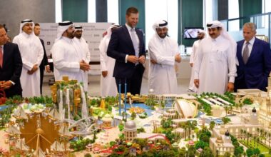 Eric Trump is examining a detailed scale model of a development project alongside several Qatari officials dressed in traditional white garments
