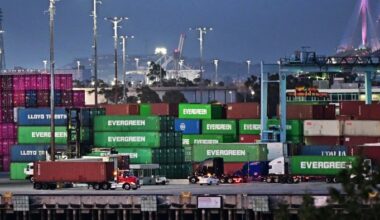 Container trucks are seen driving past stacks of shipping containers at the Port of Los Angeles