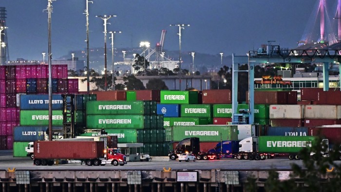 Container trucks are seen driving past stacks of shipping containers at the Port of Los Angeles