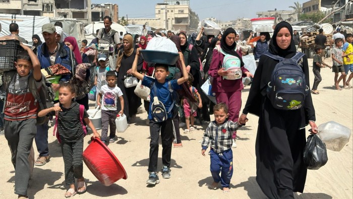 Men, women and children carry their belongings as they walk on a sandy street