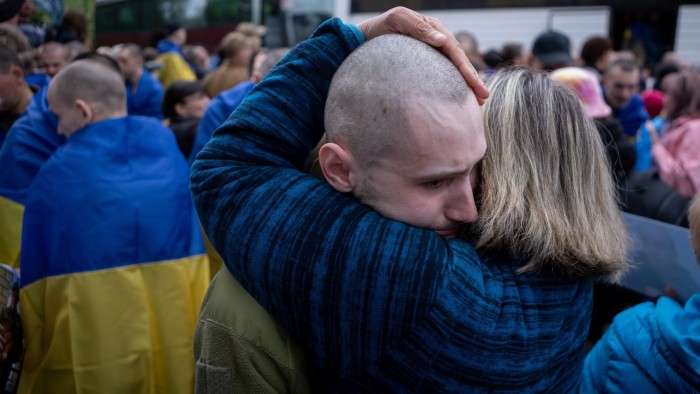 A woman embraces a Ukrainian soldier who has been released from Russian captivity, surrounded by a crowd draped in Ukrainian flags