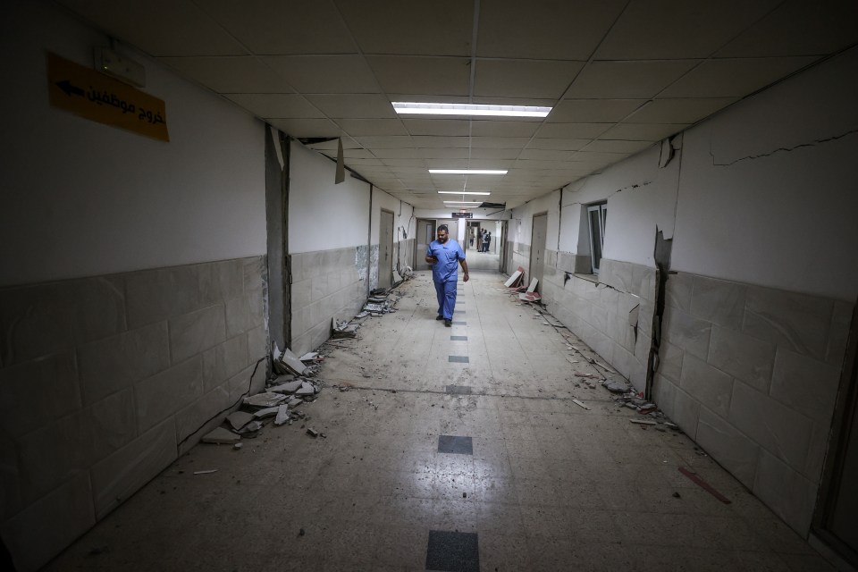 Destroyed hospital hallway with debris and a person walking through.