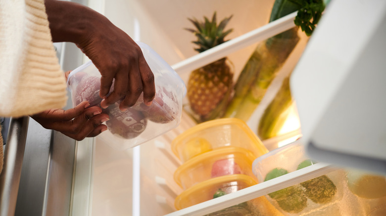 person putting something into Interior of fridge