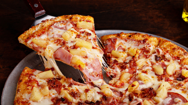 Hawaiian pizza slice being served from a whole pie