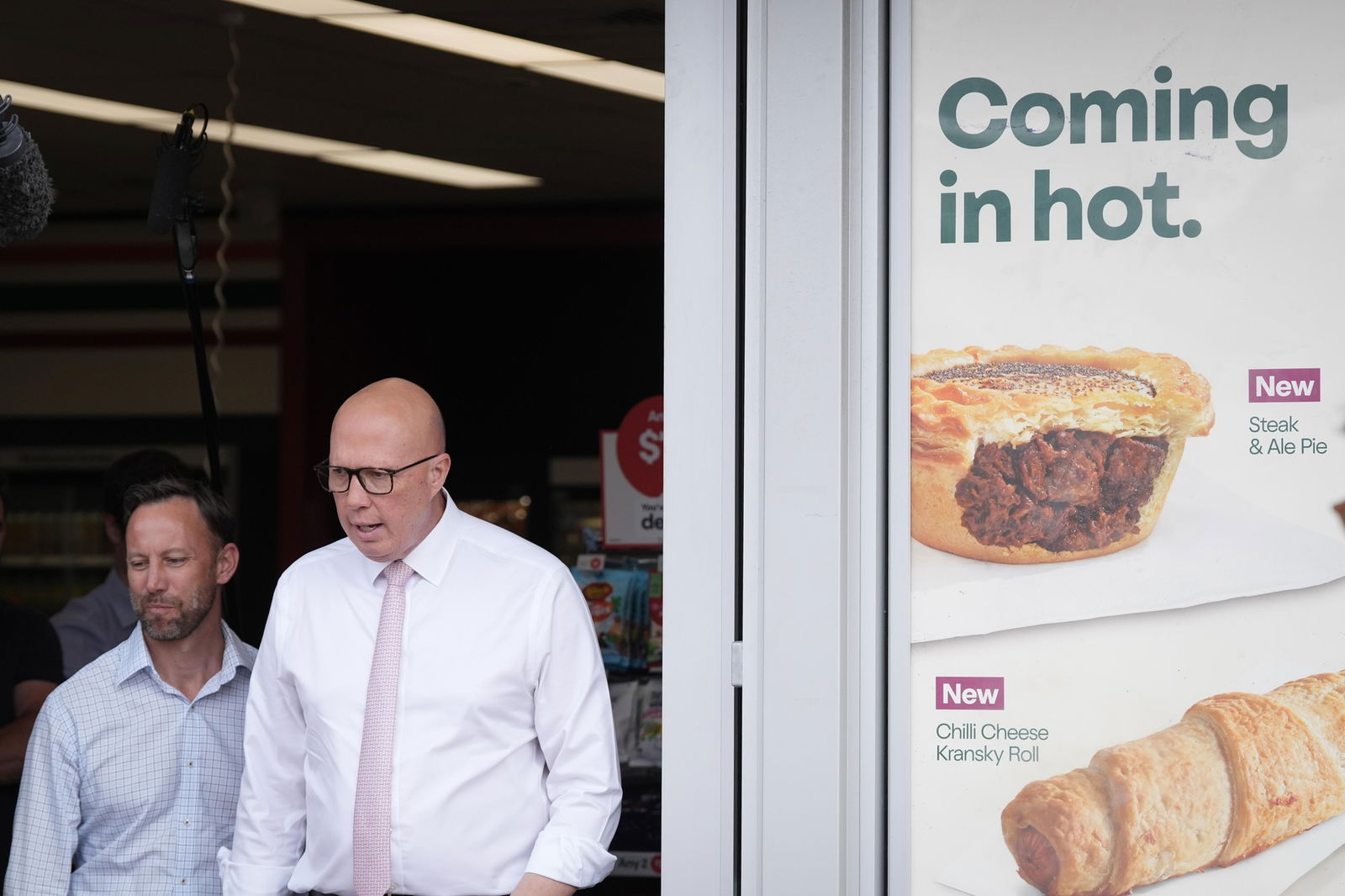 Peter Dutton walks out of a petrol station, past an ad saying "coming in hot".