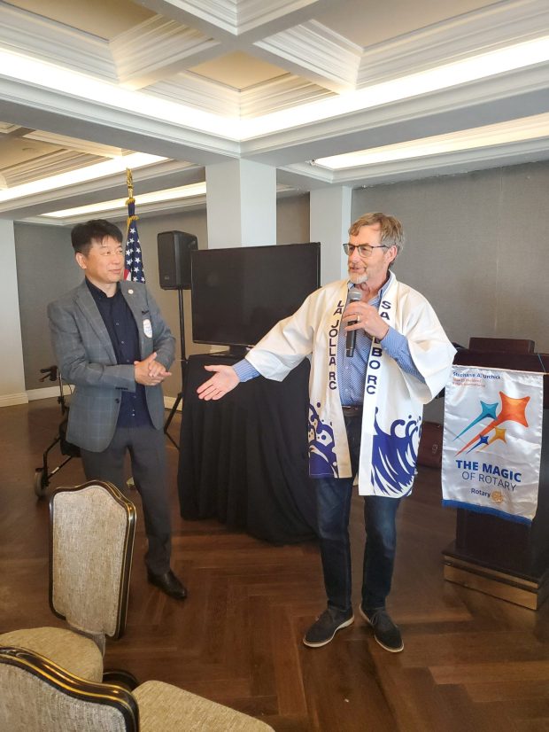 Japanese Rotarian Takahide Serino stands with Rotary Club of La Jolla member Bill Burch as Burch shows off a Rotary-themed garment he got while on a trip to Sasebo, Japan, in 1997. (Ashley Mackin-Solomon)