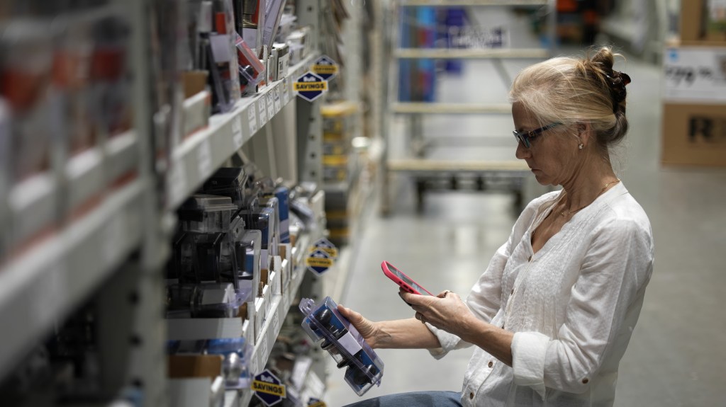 Mature woman using smart phone to photograph door knobs in a hardware store for home renovation project