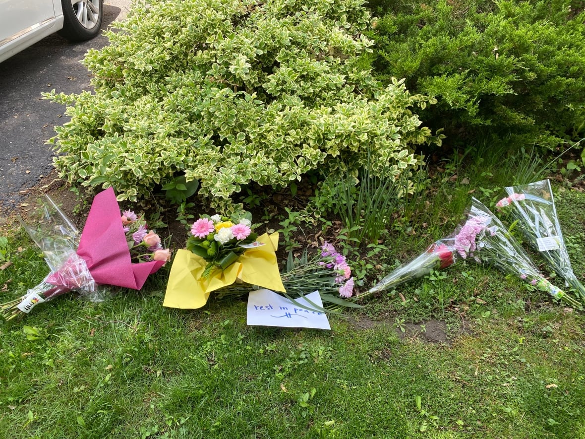 Photo showing several flowers on a lawn next to a sign reading "rest in peace."