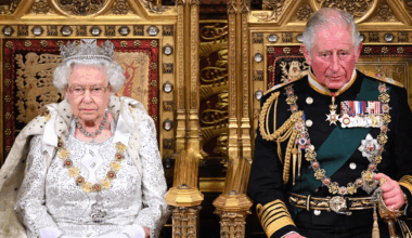 Queen Elizabeth and King Charles both wear ceremonial robes and sit on gold thrones