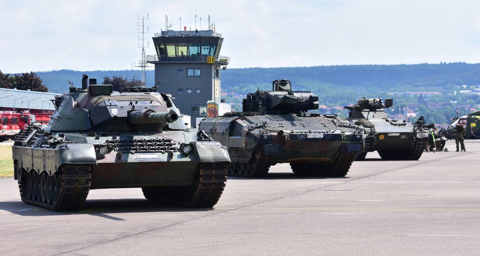 Panzer der Bundeswehr stehen nebeneinander geparkt auf einem Flugplatz. Dahinter sieht man den Tower.