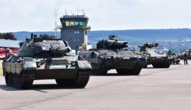 Panzer der Bundeswehr stehen nebeneinander geparkt auf einem Flugplatz. Dahinter sieht man den Tower.