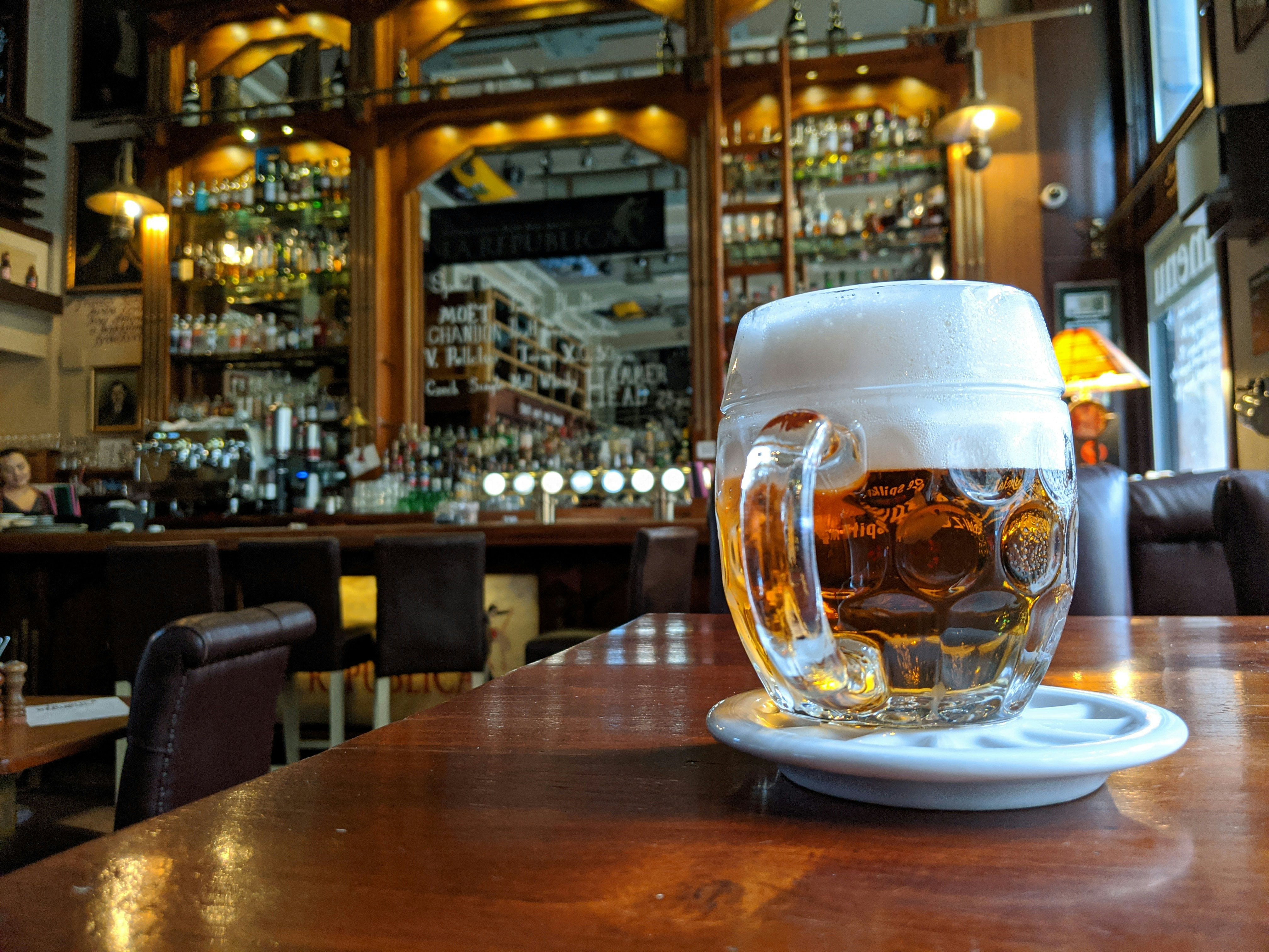 A large glass of beer with a frothy head on a table in a bar