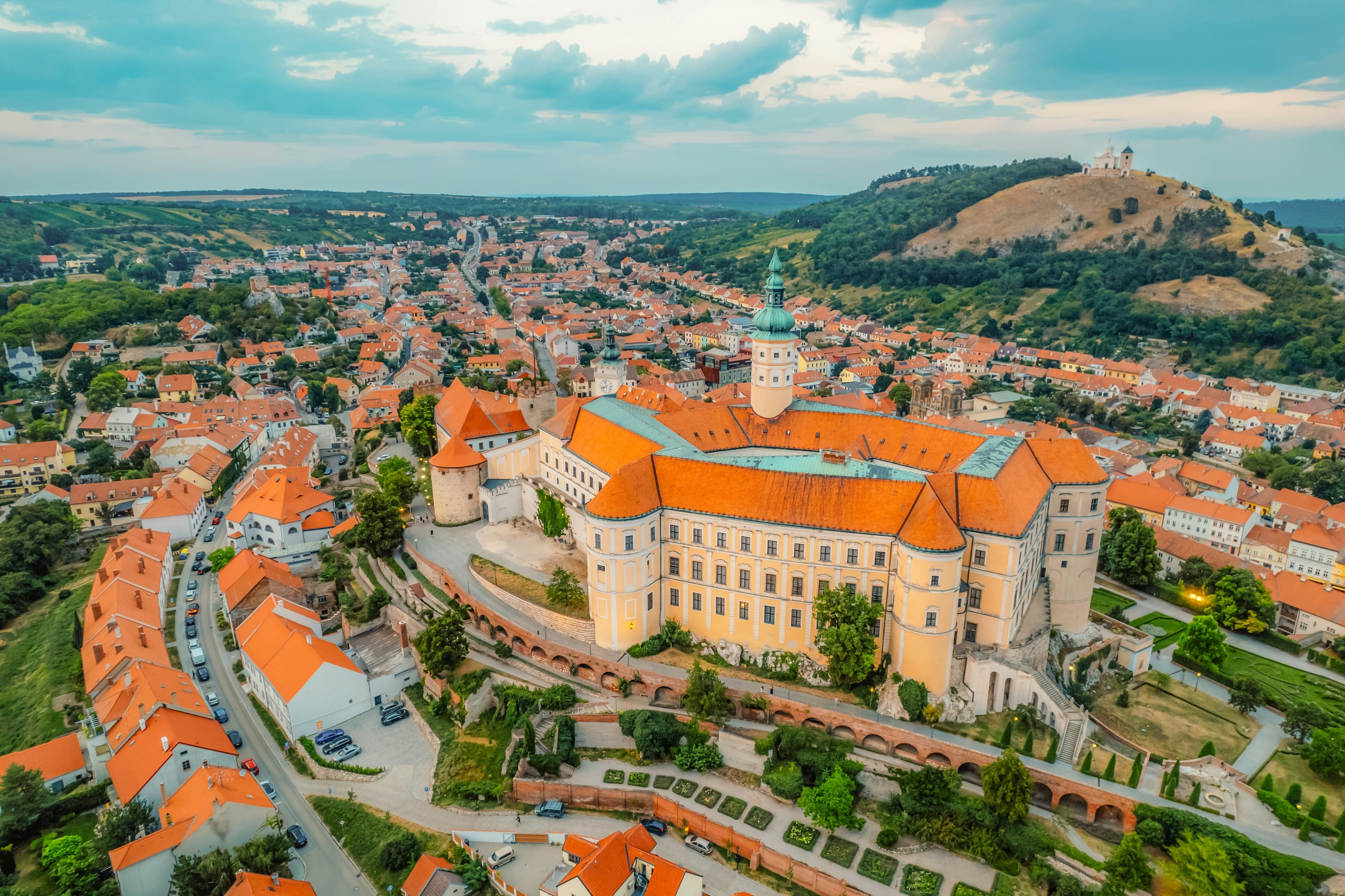 A red-roofed castle in the center of an old town with a domed church on a distant hill