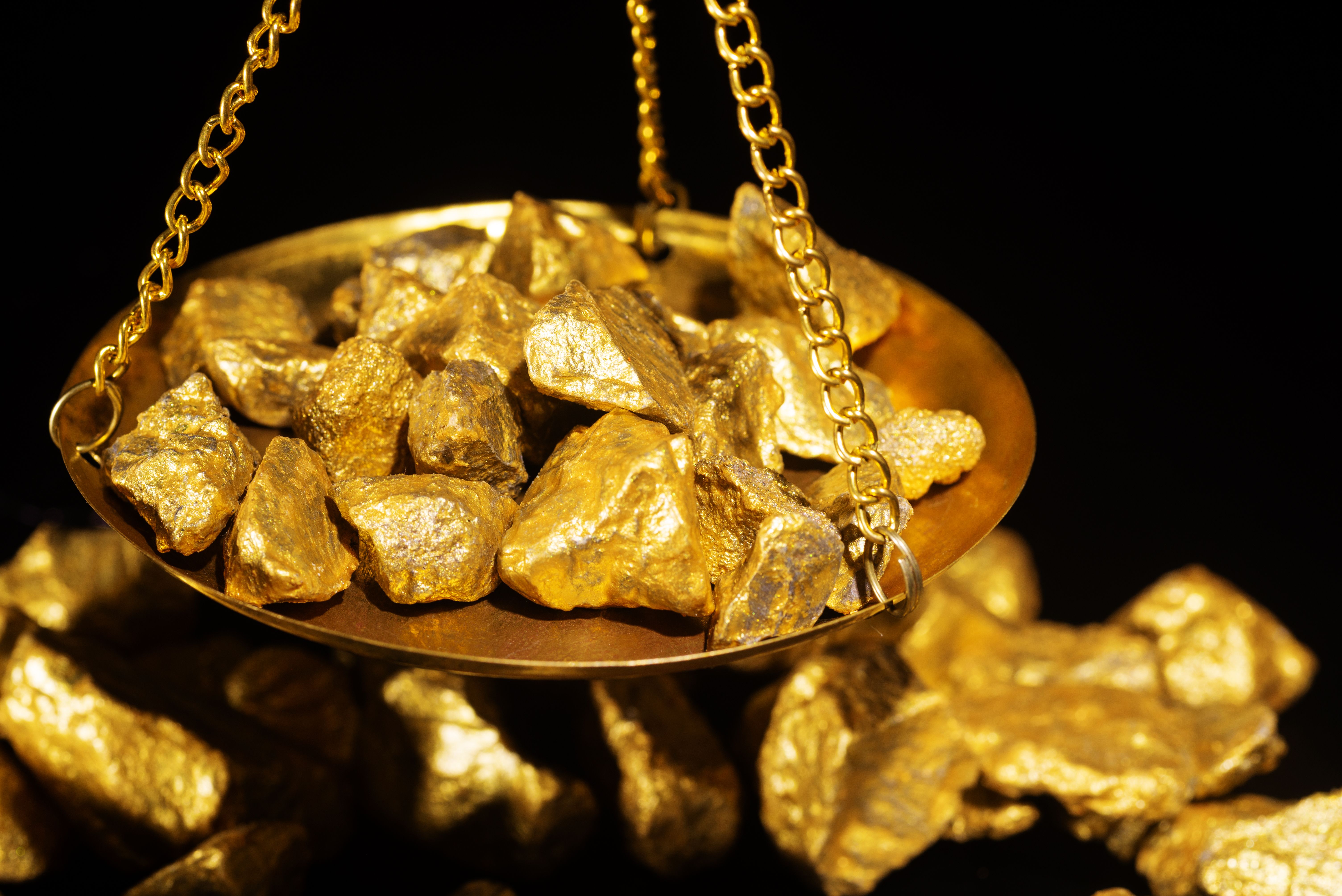 Gold nuggets displayed on a golden scale with more gold in the background