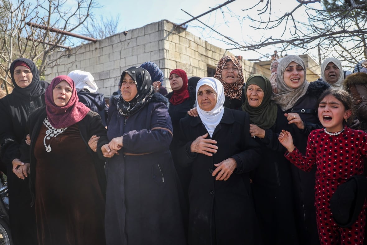 Women stand close to each other during a funeral procession.