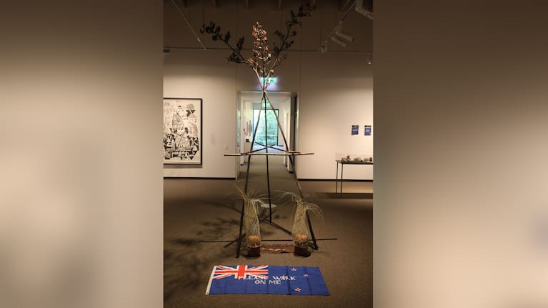 The artwork features a surveyor's tripod made from flax stalks to symbolise Māori reclamation of their land.
