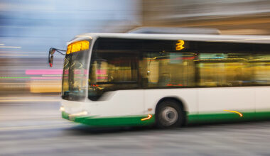 A white and green city bus in motion, captured with a blurred background to show speed, driving through an urban setting.