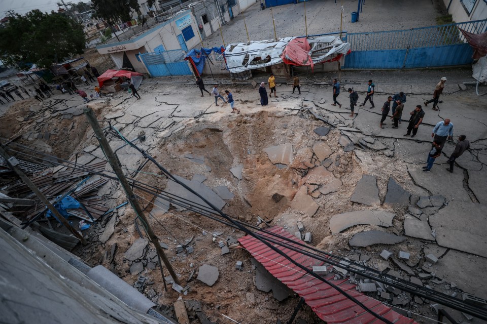 Destroyed courtyard of a hospital in Khan Yunis, Gaza, with people walking amidst the rubble.