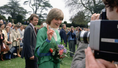 Princess Diana wearing a green dress waving her finger at the camera as a man takes a video of her