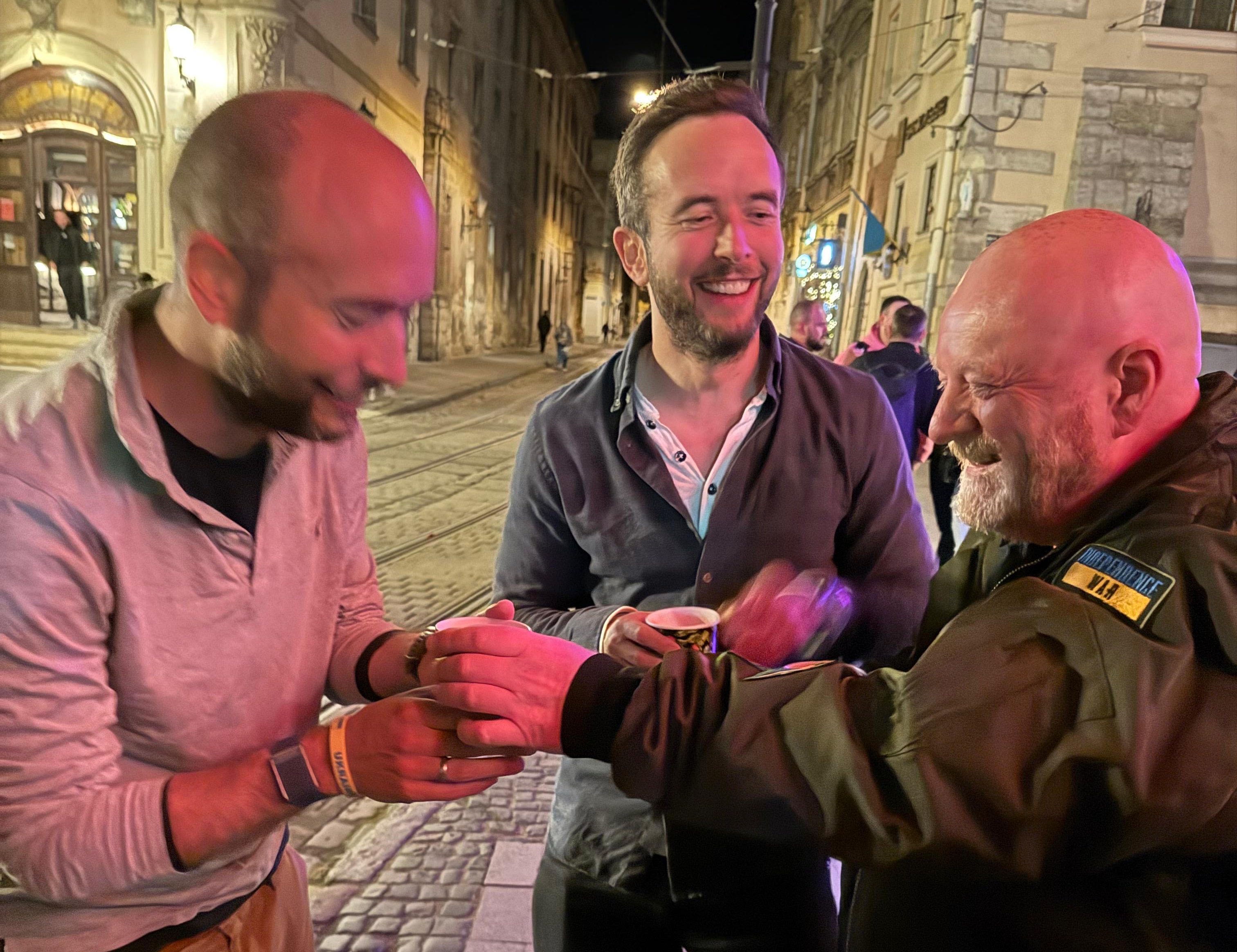 Three men sharing drinks on a city street at night.