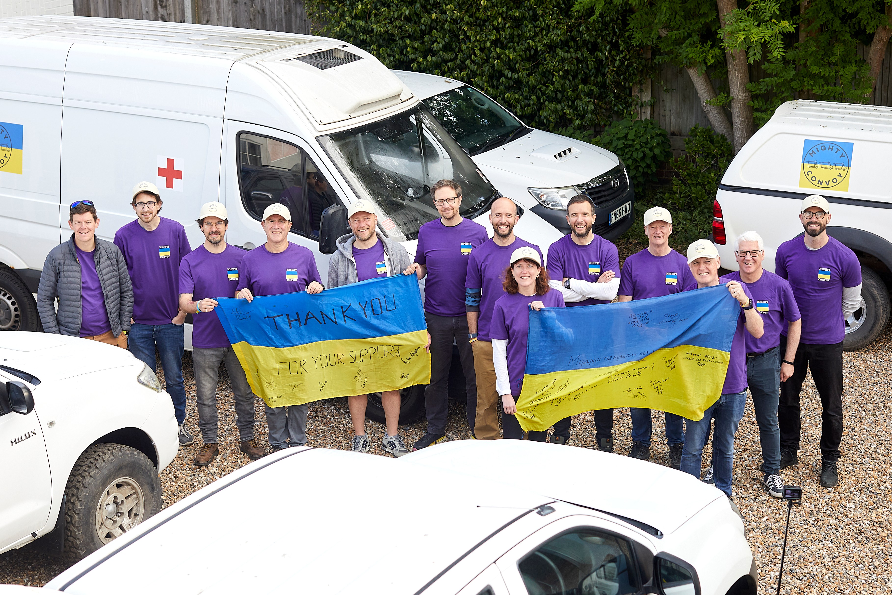 Team of people holding Ukrainian flags next to ambulances and trucks for Mighty Convoy charity.