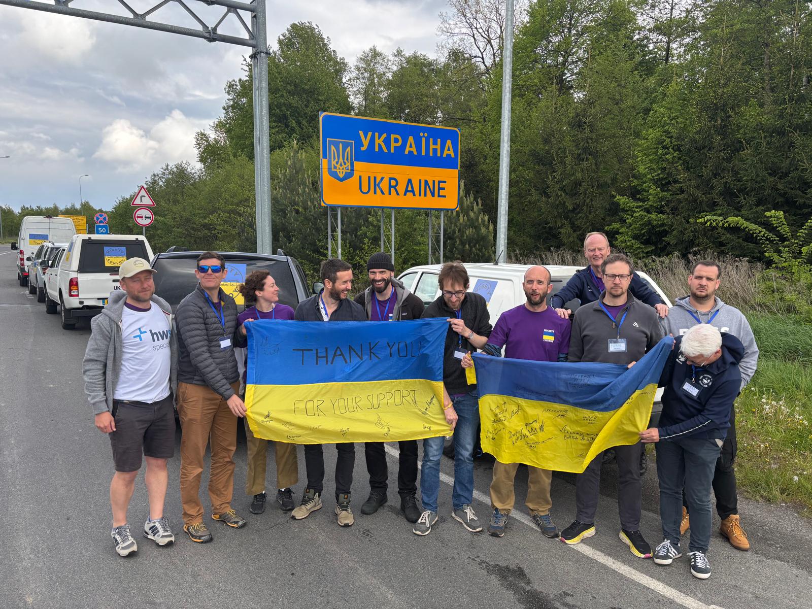 Group of people holding a Ukrainian flag that says "Thank you for your support" at the Ukraine border.