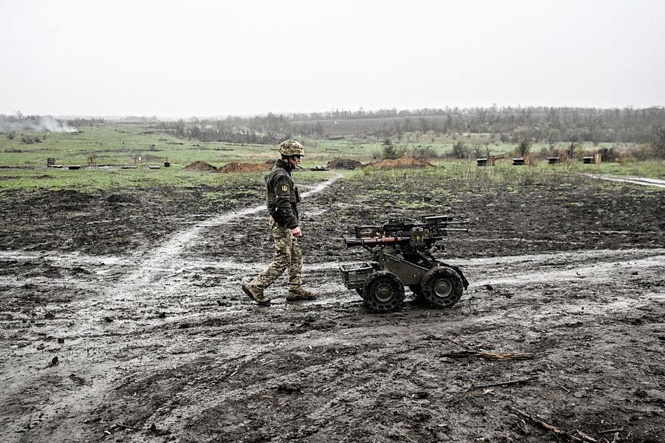 A soldier walks through a muddy field with an uncrewed ground robot.