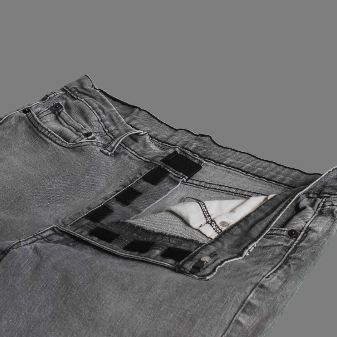 A pair of light gray jeans with the zipper partially open, showing the white inside pocket and waistband details, on a plain gray background.