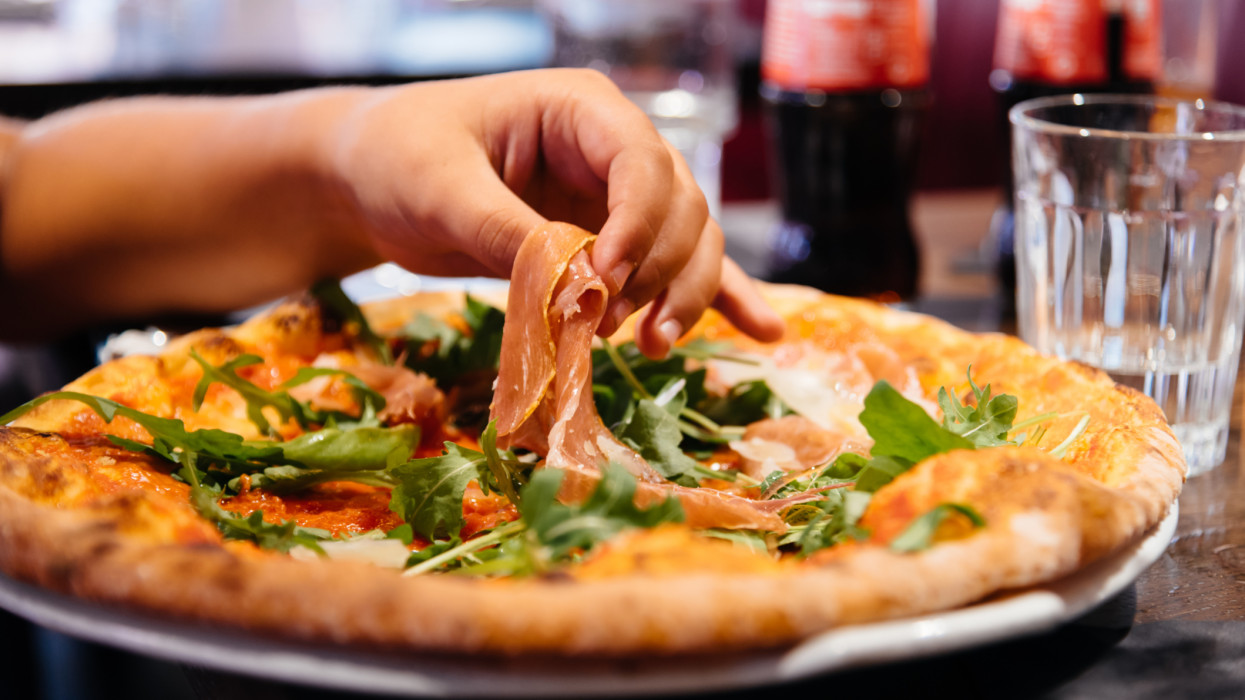 Női kéz veszi ki a sonkadarabokat a pizzatányérból egy étteremben.