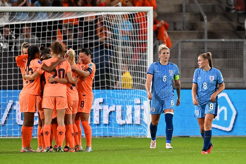 Dutch players celebrating in a huddle while two English players look on.
