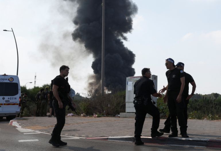 Police officers stand at a site, as smoke rises following a missile attack from Iran, in Herzliya, Israel, June 17, 2025