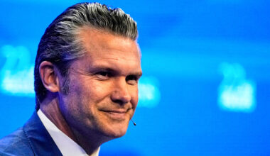 US Defense Secretary Pete Hegseth smiles on stage whilst deivering a speech