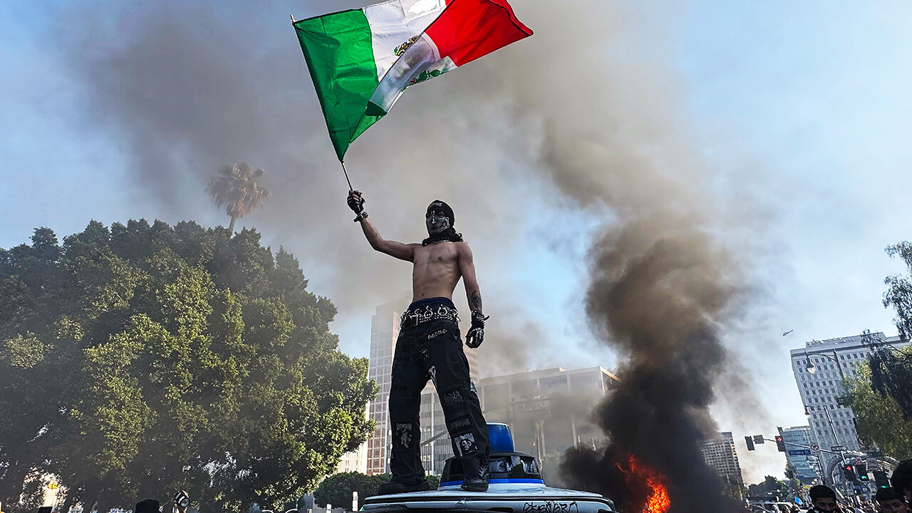 A protester holds a Mexican flag while standing on a vandalized Waymo car during a protest against immigration raids in Los Angeles, California, June 8th 2025