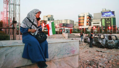 An Iranian woman sits close to a destroyed vehicle as she watches and listens to a traditional band as it performs to show solidarity with the Iranian people at Hafteh-tir Square, in Tehran