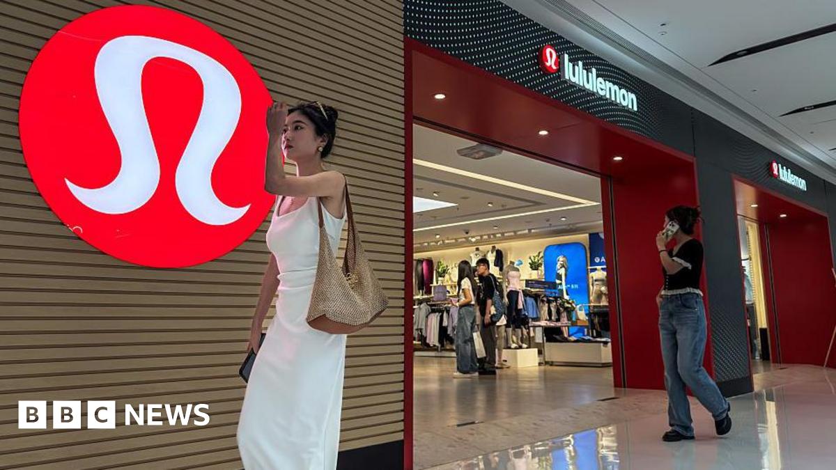 A woman in a white dress walks past a Lululemon store with its signature red logo displayed prominently on the wall, as shoppers browse inside the store, on 4 June, 2025 in Chongqing, China.