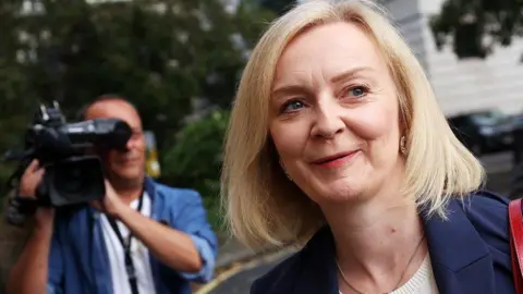 EPA A smiling Liz Truss is pictured in the street with a television camera operator visible over her shoulder. 
