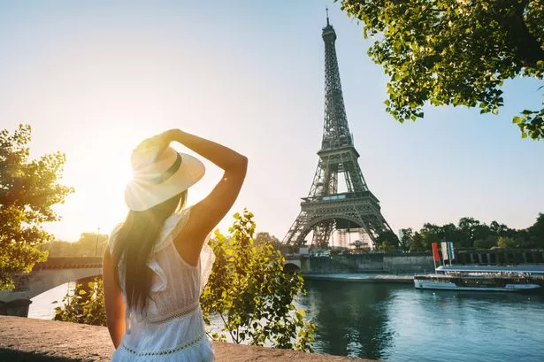 Young woman tourist in sun hat and white dress standing in front of Eiffel Tower in Paris at sunset. Travel in France, tourism concept. High quality photo