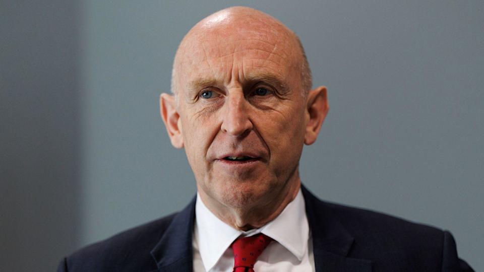 A bald headed man in a dark suit with a red tie and white shirt