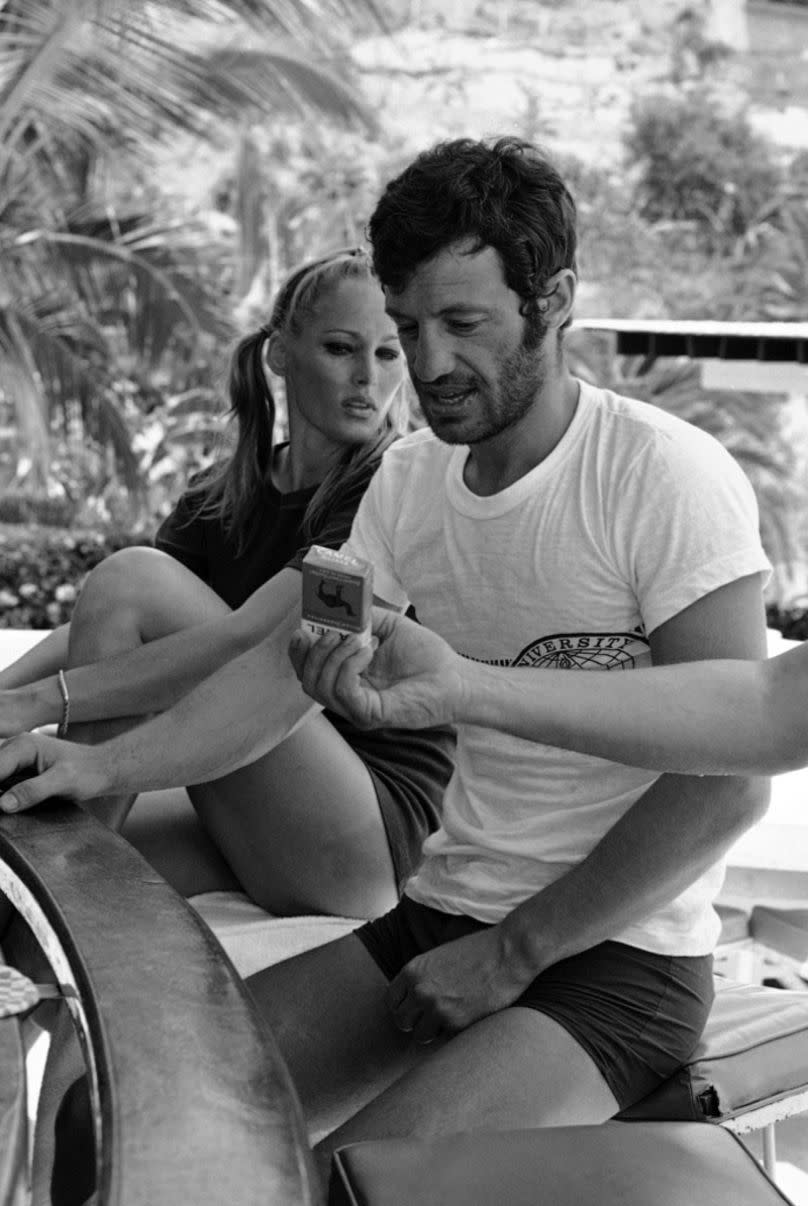 Jean-Paul Belmondo with Ursula Andress look at a pack of cigarettes that is offered to them by the bar at their hotel on 18 April 1967 in Acapulco, Mexico.