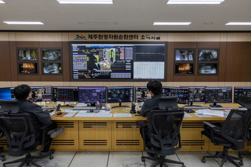 Men operate consoles in a control room. 