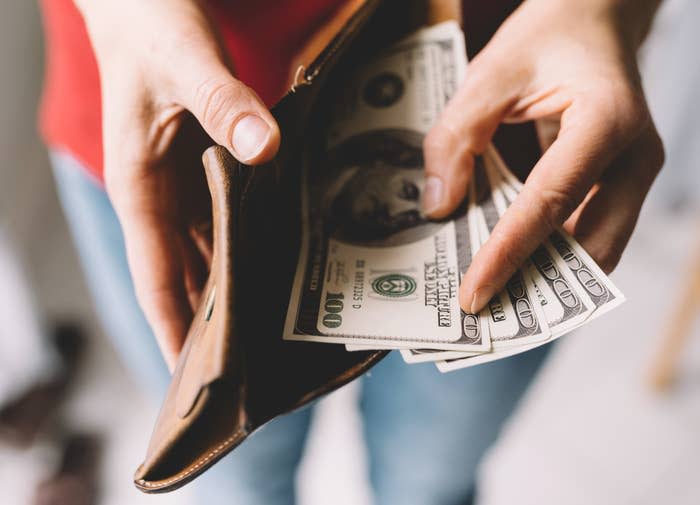 Hands holding a wallet with several U.S. hundred-dollar bills, depicting financial management or spending
