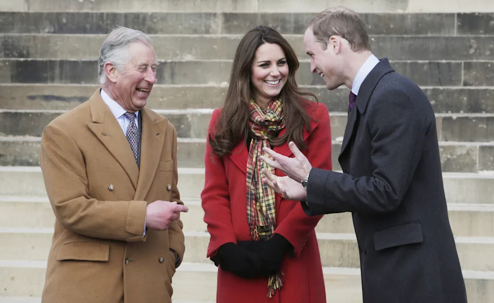King Charles wears a brown overcoat and laughs alongside Kate Middleton, who wears a red coat with a tartan scarf, and Prince William