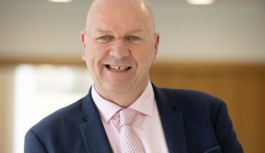 A bald man in a pink dress shirt and a blue blazer.