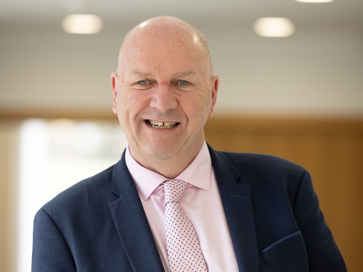 A bald man in a pink dress shirt and a blue blazer.