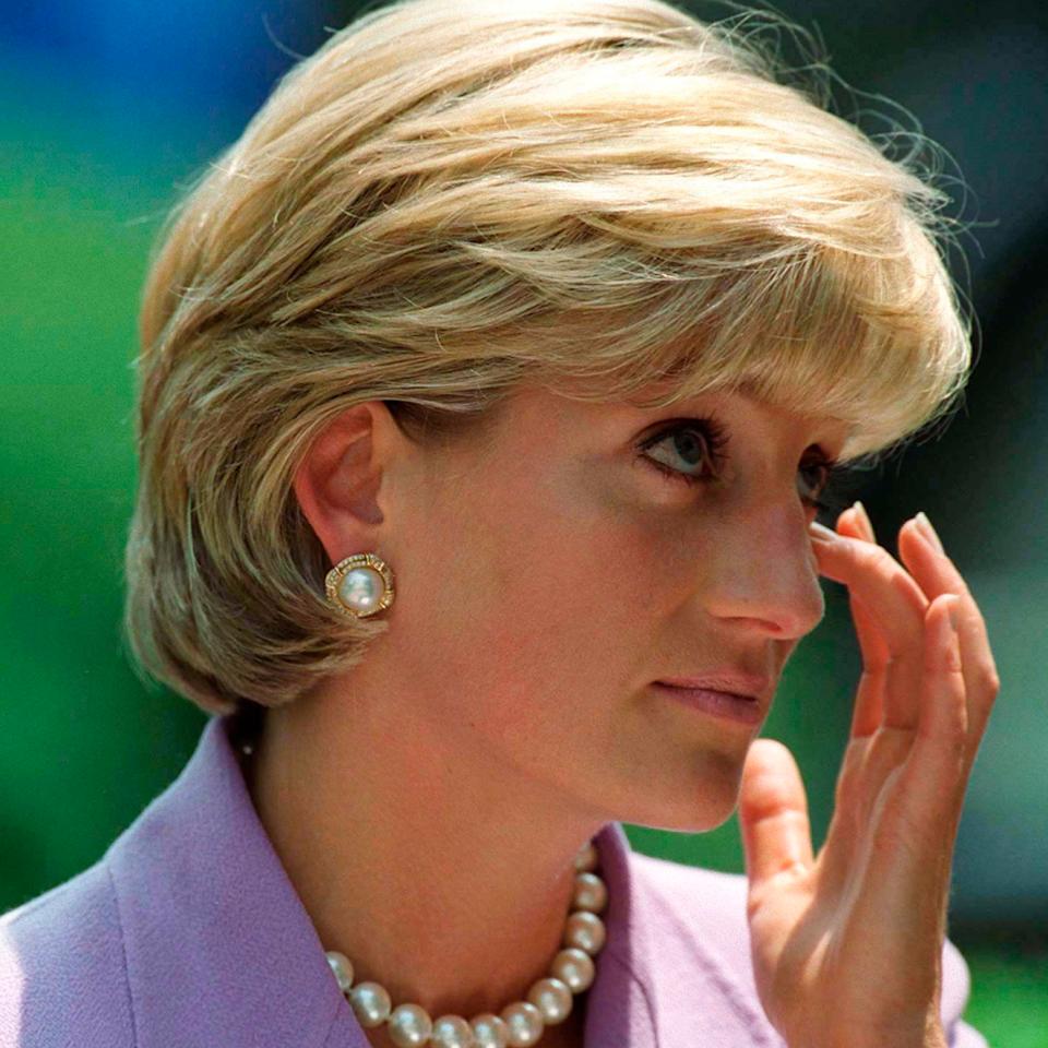 Princess Diana wearing a lavender suit and wiping her eye.
