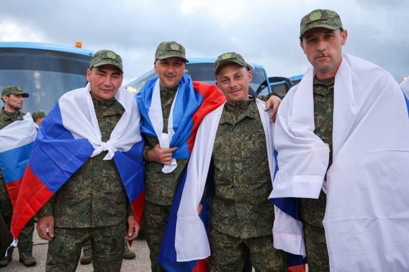 Russian servicemen released from Ukrainian captivity pose with Russian flags after their return. Alexander Patrin/TASS via ZUMA Press/dpa