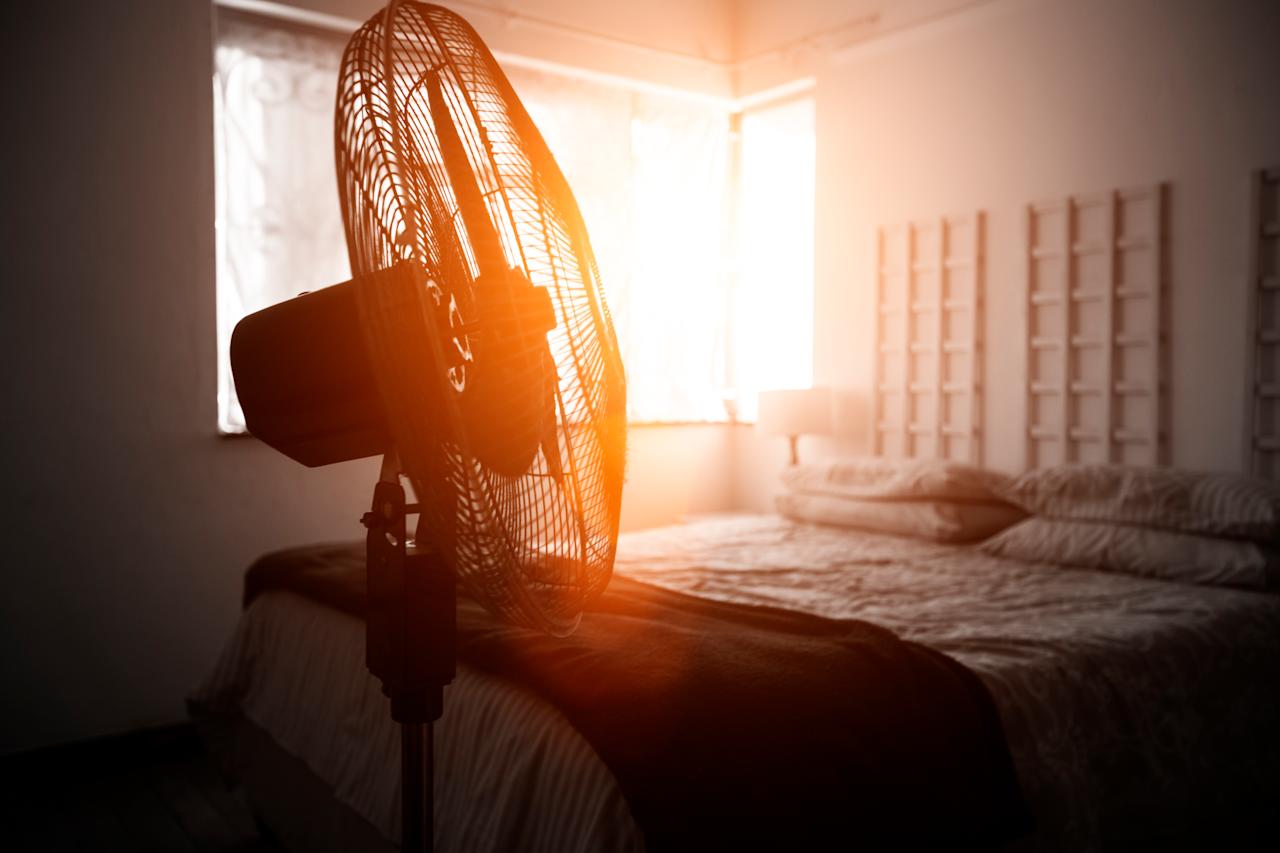 Electric fan next to bed with sunshine coming through the window.
