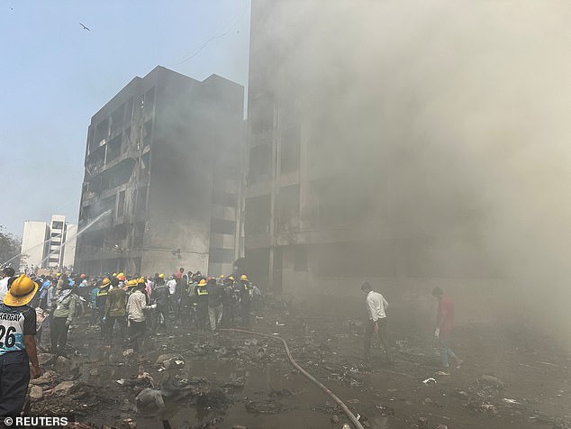 Rescue teams spray water over charred buildings as smoke rises at the Air India crash site
