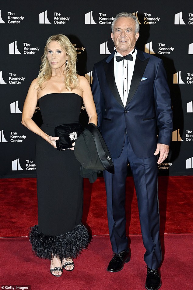 Health Secretary Robert F. Kennedy Jr. wore a similar blue tuxedo, however, his white button-down shirt underneath contained piercing black stripes. His spouse, Cheryl Hines opted for a $298 Mac Duggal black midi dress. The strapless number contained an eye-popping feathered fringe at the bottom of the skirt