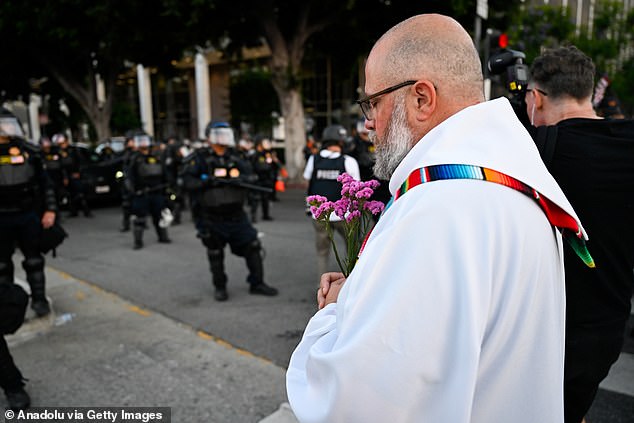 A priest holds flowers as police confront with anti-ICE protesters near Federal Building and Metropolitan Detention Center in Los Angeles, California on June 10, 2025 amid protests over immigration raids